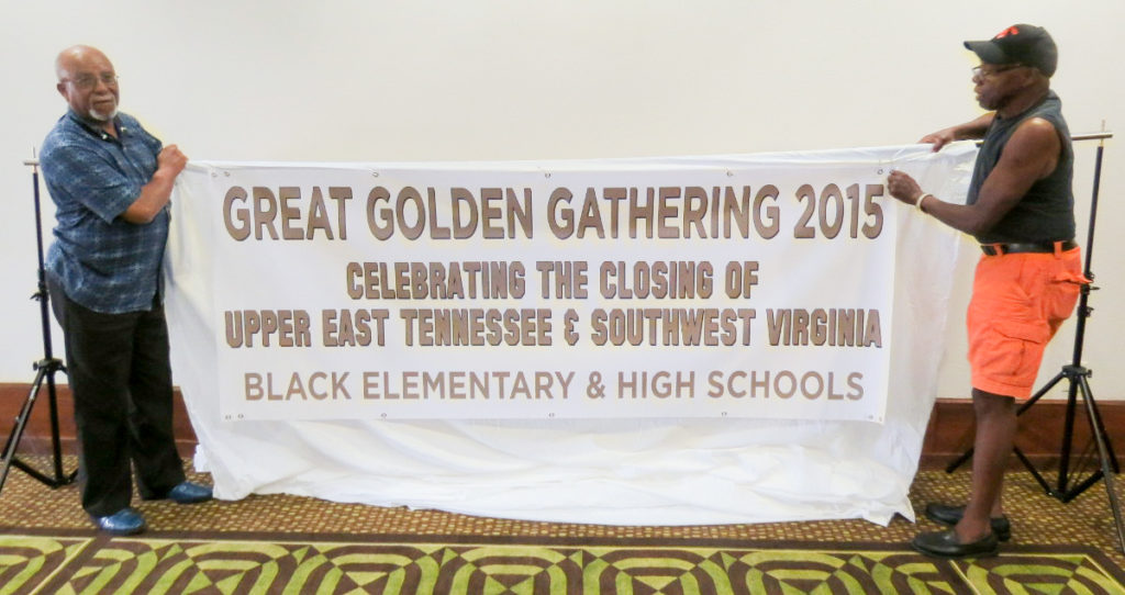 Two alumni hold a large white banner with gold lettering announcing the Great Golden Gathering 2015.