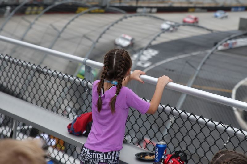 A young girl with long braids stands up in her seat to take in the view of a NASCAR race at Bristol Motor Speedway.