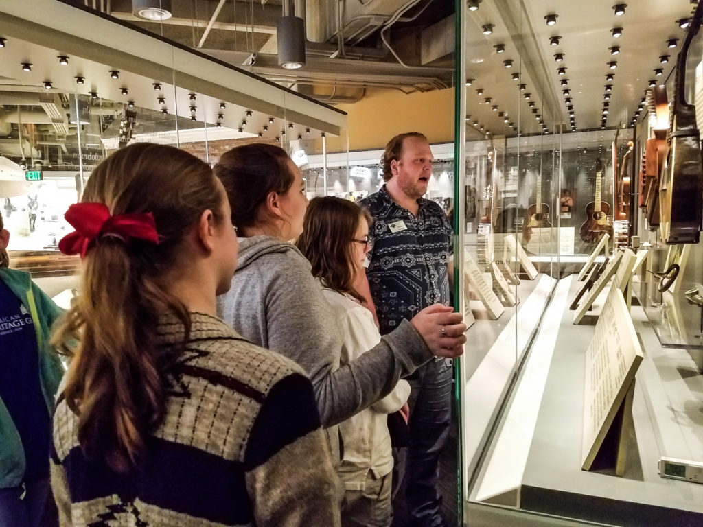 Museum staff member showing a group of female students the instruments in the museum's permanent exhibits.