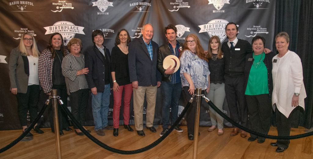 Several members of the BCM staff pose with Ken Burns and his creative team in front of a branded backdrop with the logos for BCM, the museum, Bristol Rhythm &  Roots Reunion, and Radio Bristol.