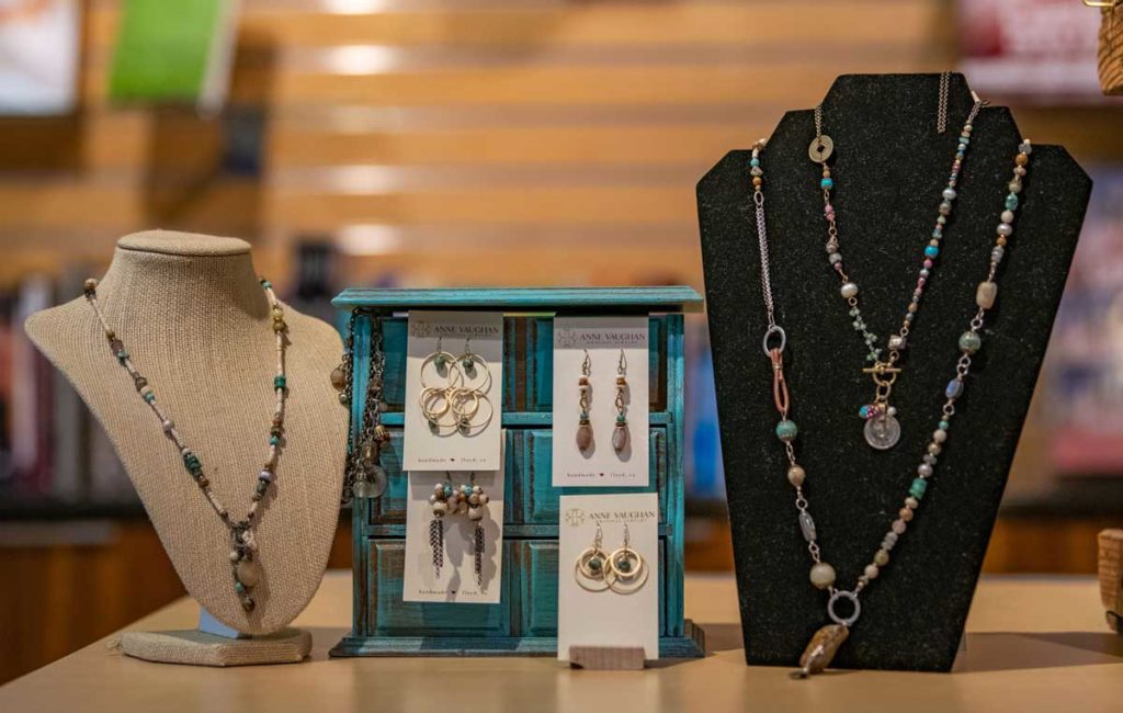 Two display forms adorned with colorfully beaded chains with stone and coin pendants and a smaller display of long earrings that coordinate with the necklaces.