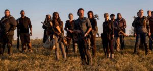 Several cast members of the show The Walking Dead standing in a field at sunset holding weapons as if they are ready for battle.