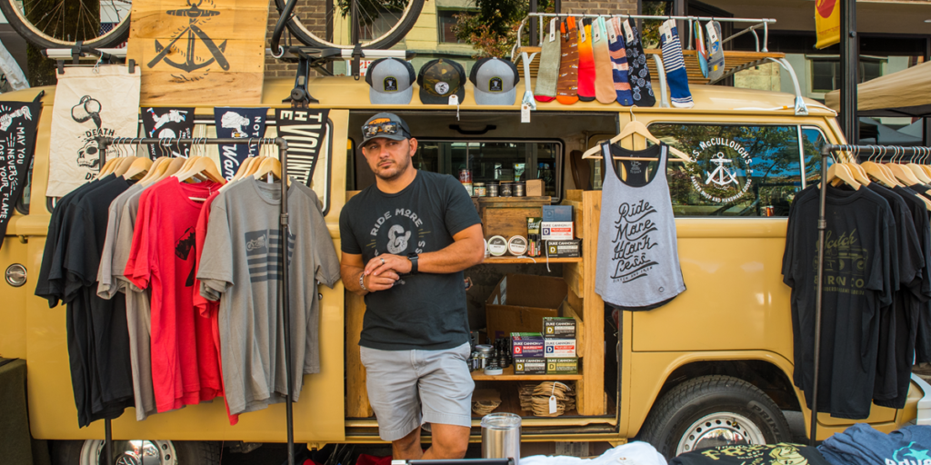 The Fouled Anchor's VW bus booth with the vendor standing out front with his wares displayed around him.