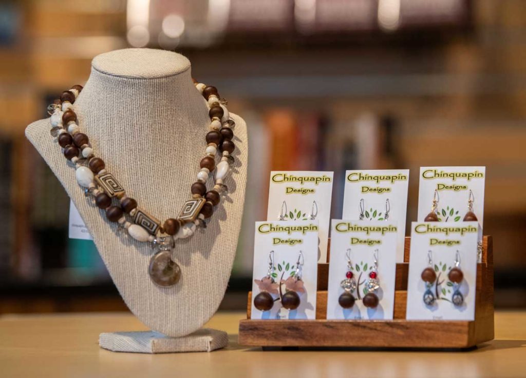 A lovely chinquapin beaded necklace interlaced with white beads and a fossil pendant on a display form beside a smaller display of long chinquapin beaded earrings by Chicuapin Designs.