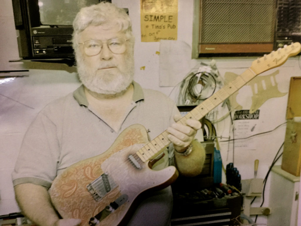 Chuck Tipton holding an electric guitar, covered in a paisley design.