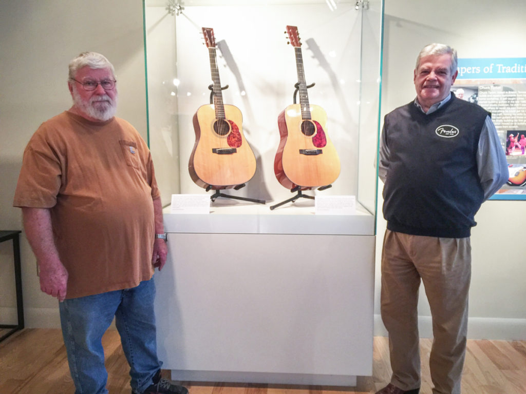 Chuck Tipton to left and Doug Sims to right, in front of the museum case displaying two of Tipton's guitars.