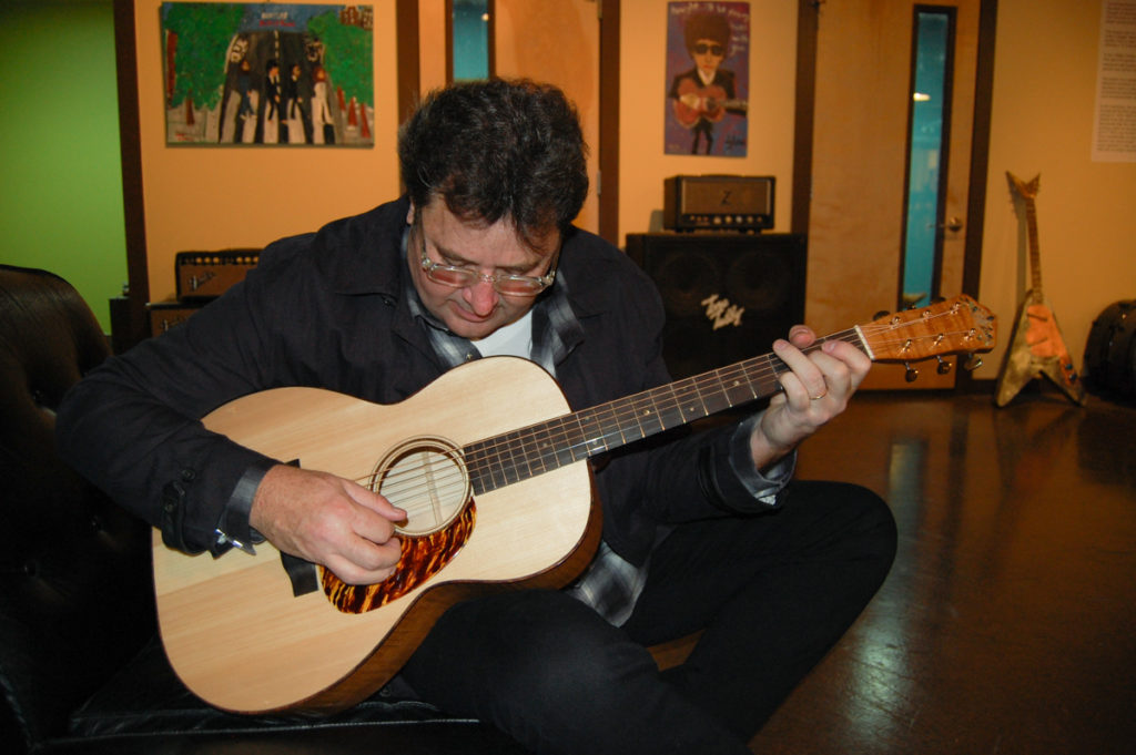 Vince Gill, wearing mostly black, playing the Doc Watson guitar in what looks to be a studio or green room space.