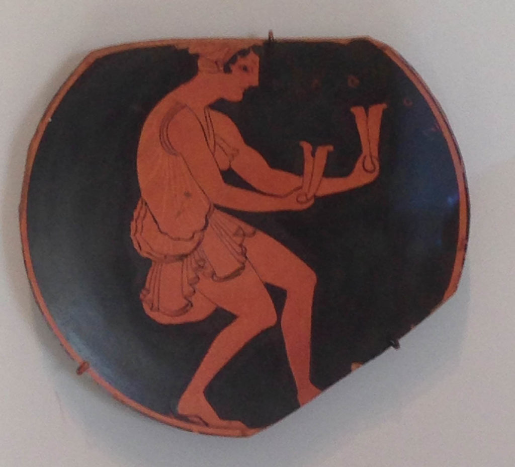 A pottery sherd with a red-figure dancer, gender unclear holding two bones-like instruments in their hands.