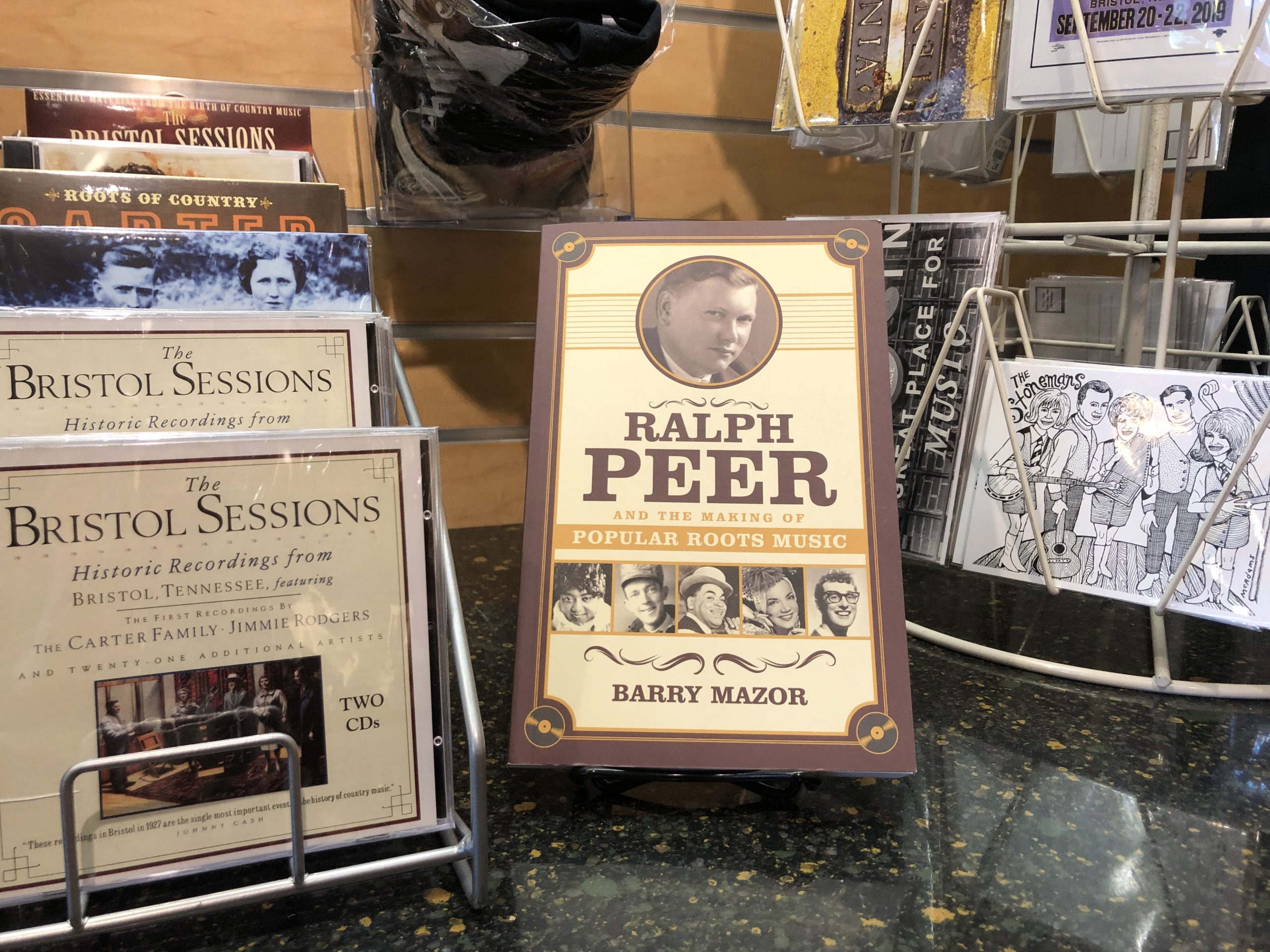 The book is on display in front of a postcard rack with a Stonemans postcard and beside of a CD display, including CDs of the Bristol Sessions and The Carter Family.