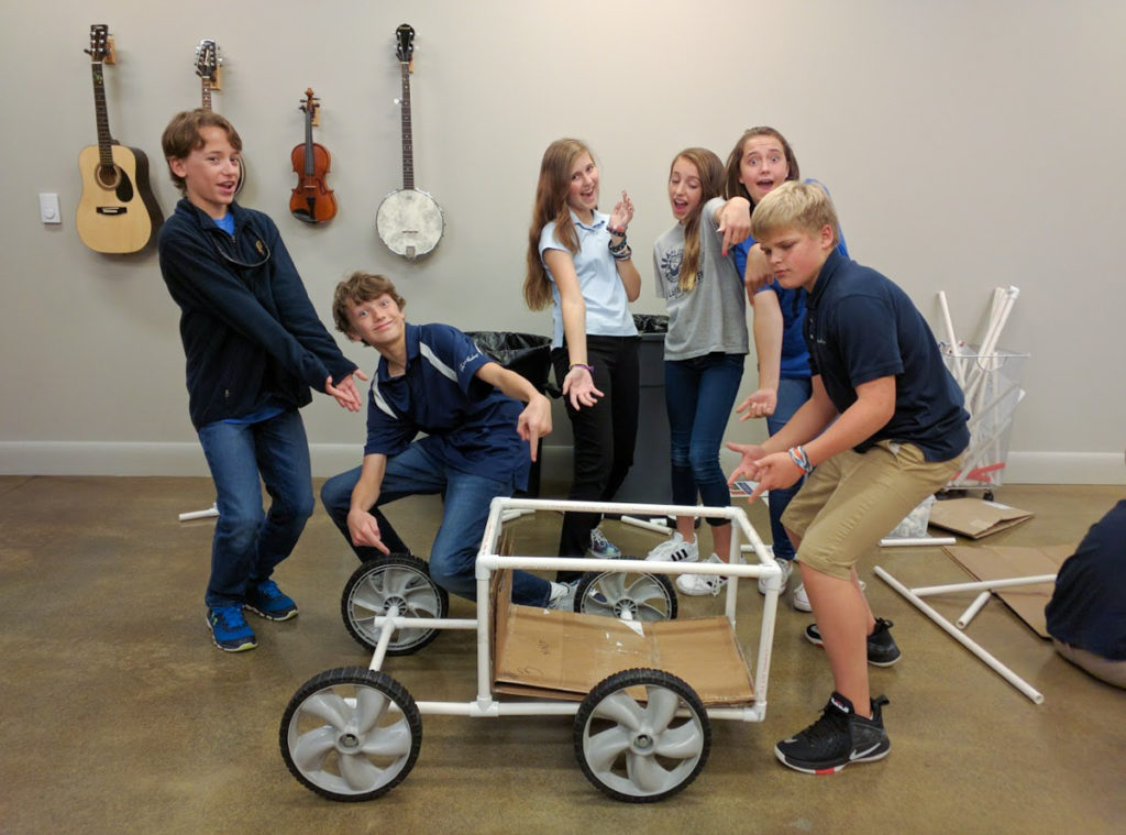 A group of students grouped around their finished Invent-a-Vehicle, all making silly faces and poses!