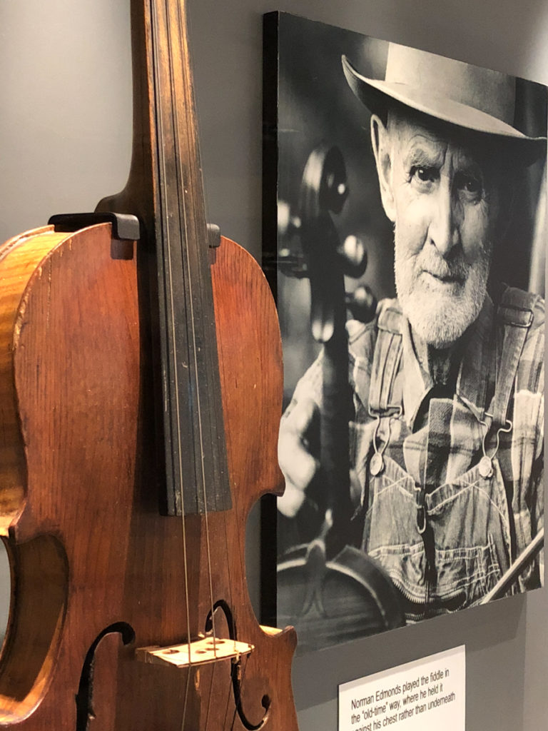 Photograph of museum case displaying an old fiddle and a photograph of Norman Edmonds, holding his fiddle.