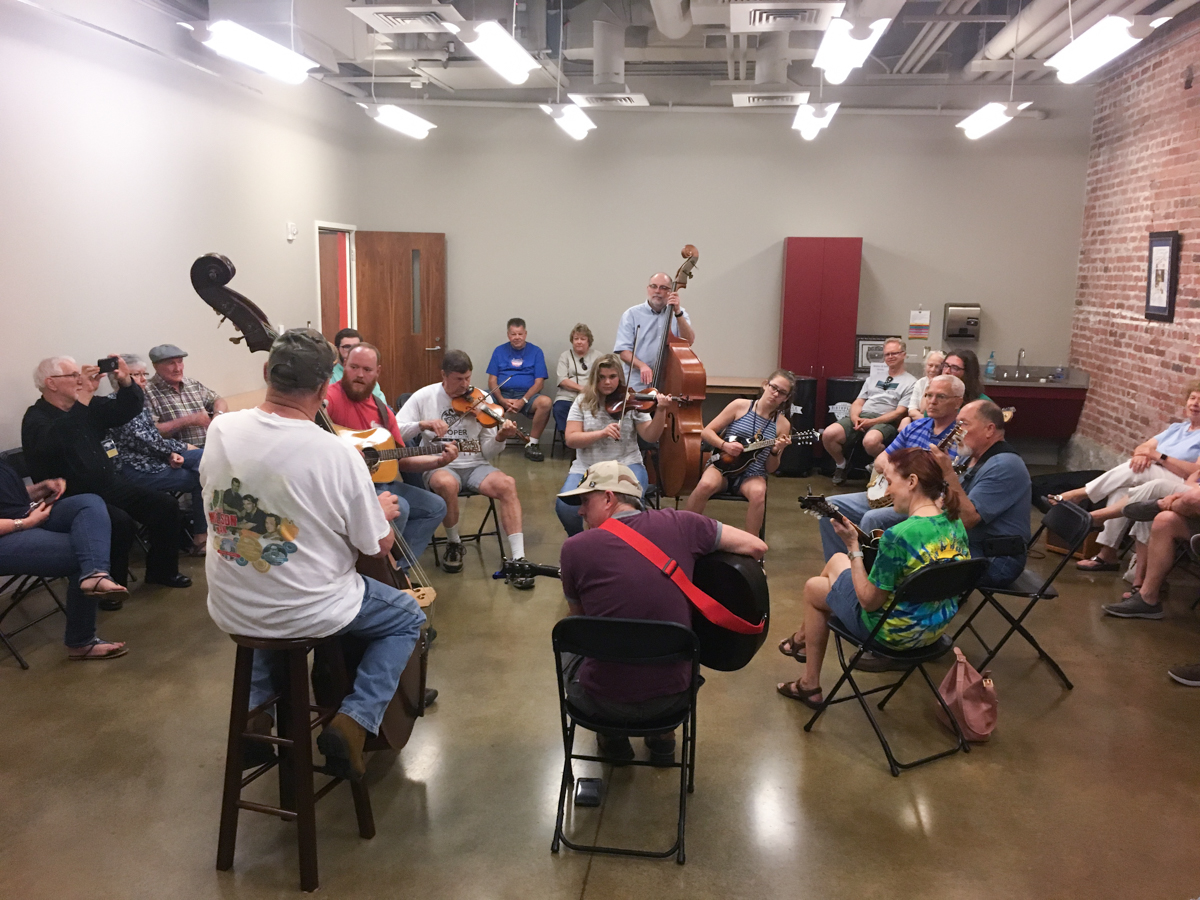 A photograph of a group of jammers in the museum's Learning Center -- they are arranged in a circle of about 10-12 musicians.