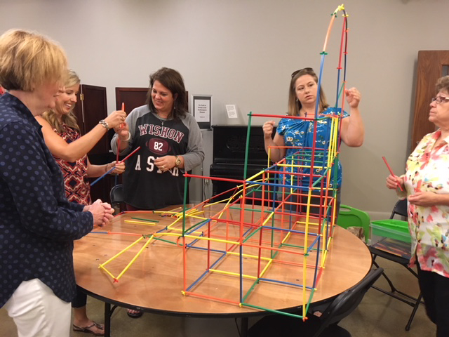 Group of teachers working together at a round table to build a structure of colorful straws.