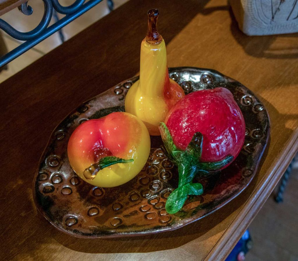 A ceramic tray holding a blown glass peach, pear, and strawberry made by Glass by Glass Studios.