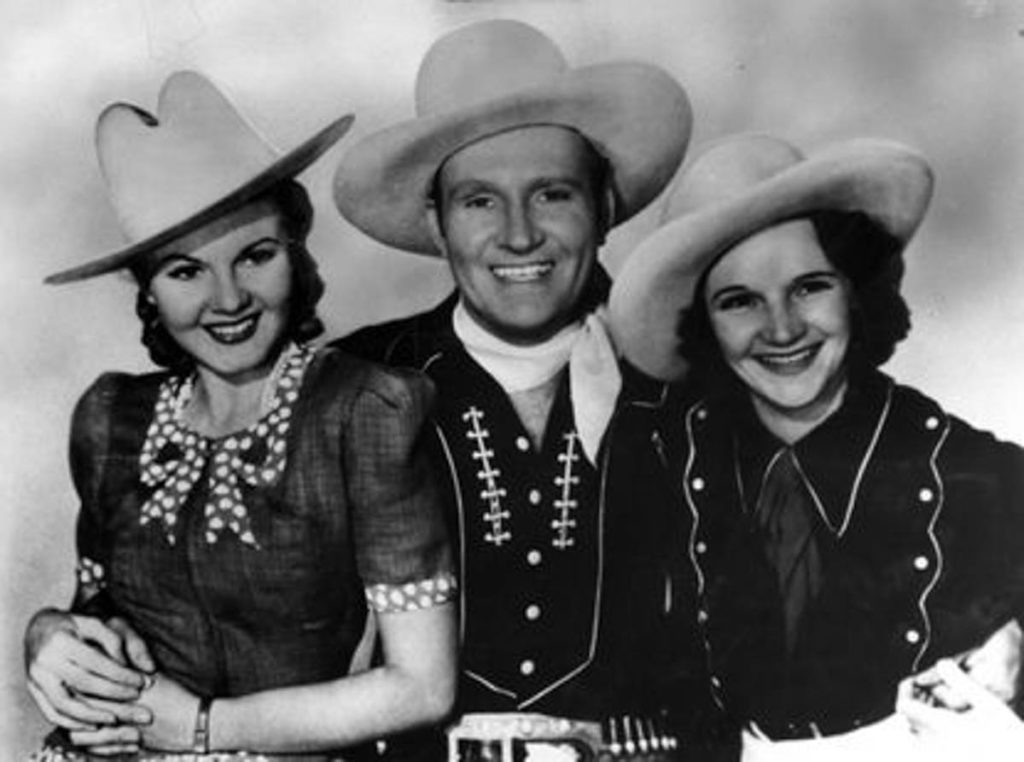 Gene Autry with June Storey to the left and Patsy Montana to the right, all three wearing cowboy hats and cowboy/cowgirl outfits.