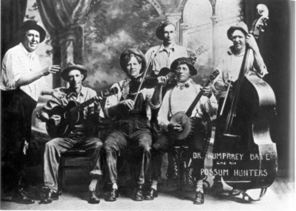 Black-and-white image of Dr. Humphrey Bate and His Possum Hunters, 6 band members all dressed in country or rural-style clothes, including suspenders, floppy hats, and work pants.