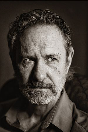 A black-and-white portrait of the author Ron Rash, looking grizzled and contemplative.
