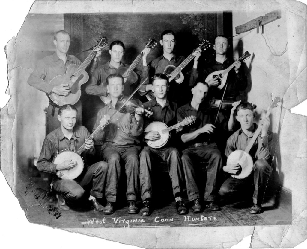 Full group of West Virginia Coon Hunters band: Belcher, Meadows, and Brown are holding guitars; Vest is holding a mandolin; Stewart, Mooney, and Stephens are holding banjos; and Boyles and Pendleton are holding fiddles.
