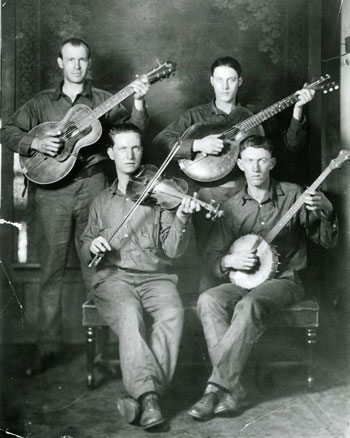 Four members of the West Virginia Coon Hunters: two standing with guitars, and two sitting, one with fiddle and one with banjo.