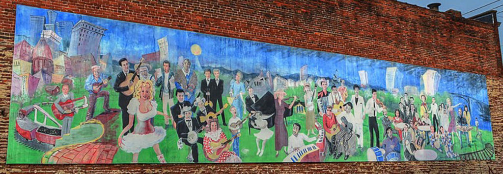 A long rectangular mural with a cityscape shown behind the people in front. Different musicians and singers are shown throughout the foreground in a folk-art type style -- some are playing instruments, others are singing.