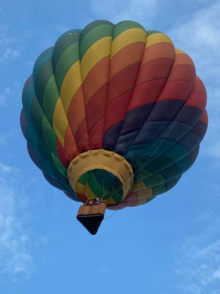 A rainbow-colored hot air balloon rises into the blue sky -- seen from below.