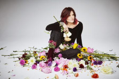 A photo of Rosanne Cash sitting among a mound of flowers.