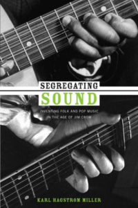Black-and-white book cover with title in the center dividing two close-up shots of a guitar player's hands on the neck of the guitar -- one hand is that of a Black musician, the other that of a white musician.
