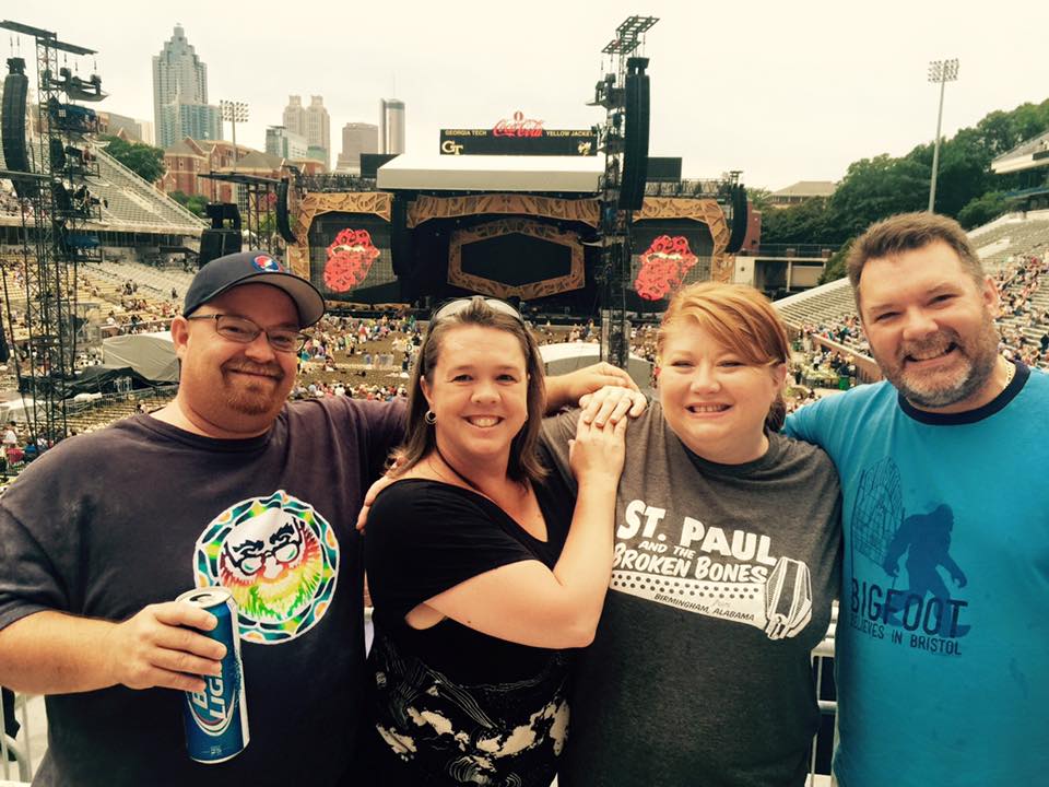 Eric Childress, Tracey Childress, Charlene Baker, and Tim Baker posing in front of the stage at Atlanta's Bobby Dodd stadium prior to St. Paul & the Broken Bones' opening performance for The Rolling Stones. Charlene is wearing a St. Paul & the Broken Bones t-shirt.