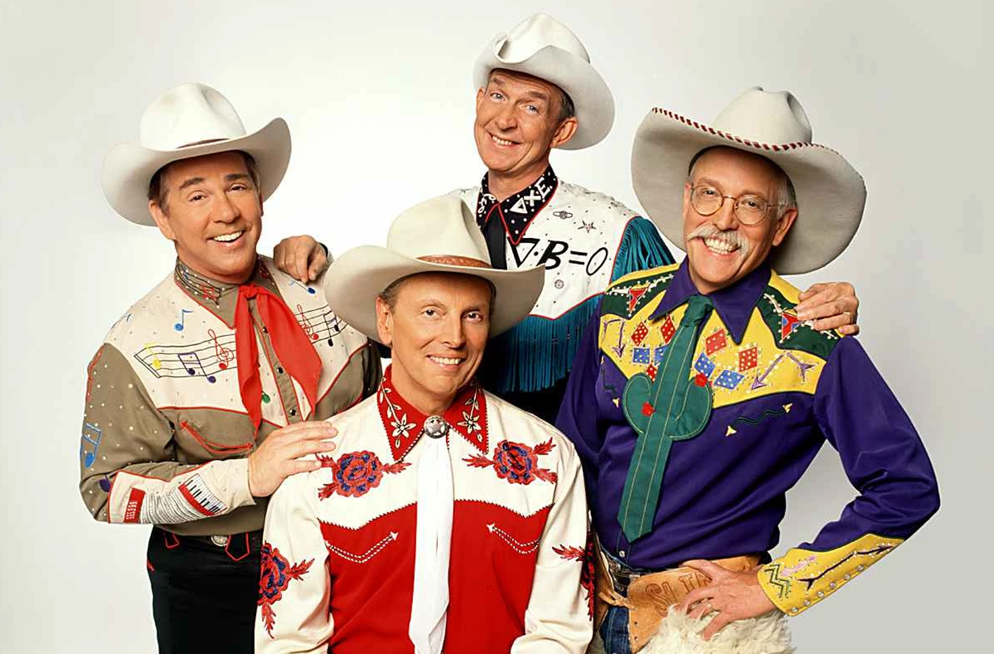 A photo of the band Riders in the Sky. Four men over a plain background wearing cowboy hats and western shirts.