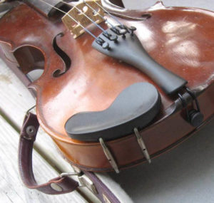 Close up of a well preserved fiddle with rich wood, looking at it from its base and up towards the neck. There is a strap attached to one side.