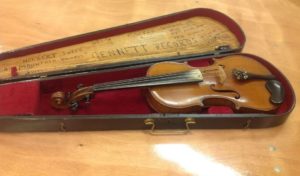 A fiddle in its case. There is writing on the top inside part of the case, and the rest is lined in red velvet.