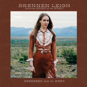 Image: Album cover has a reddish brown border around the central photograph. In the photo, a young white woman with long brown hair is walking towards the camera; she wears a reddish-brown and white prairie-style top and skirt with western belt. A landscape of scrubby brush and mountains can be seen behind her.