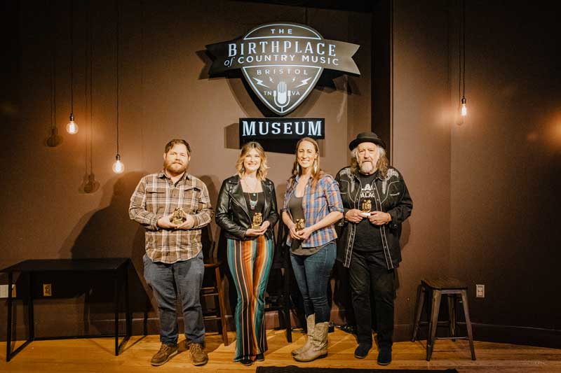Adam Bolt, Melissa Johner, Katie Powderly, and Ron Short holding their trophies under the Birthplace of Country Music Museum sign in the museum's performance theater.