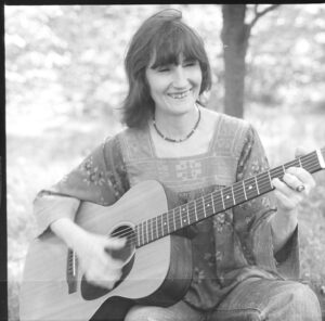 Hazel Dickens sitting down playing the guitar outside 