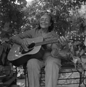 A photo of Etta Baker in her later years, holding an acoustic guitar and smiling.