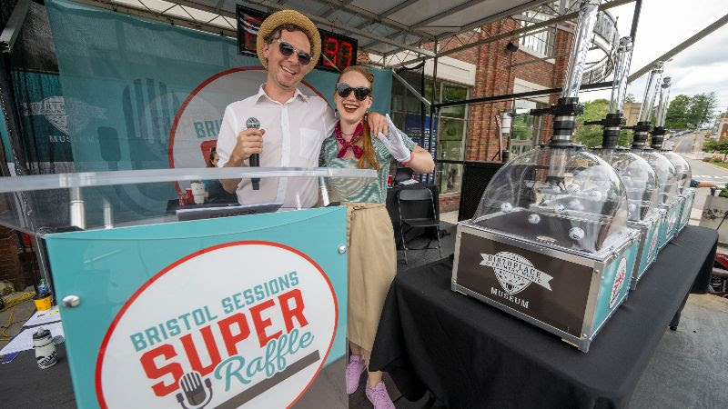 A photo of WBCM Radio's Kris Truelsen and Toni Doman hosting the Bristol Sessions Super Raffle in 2022. They are standing in the Bristol Sessions Super Raffle tent with the ball machines outside the Birthplace of Country Music Museum.