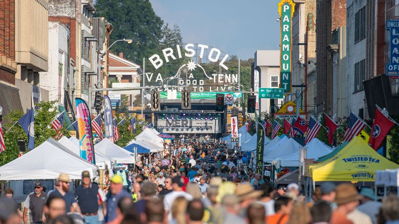 A photo of Historic Downtown Bristol, VA-TN's State Street, filled with people, with a stage in the background and the Bristol Sign.