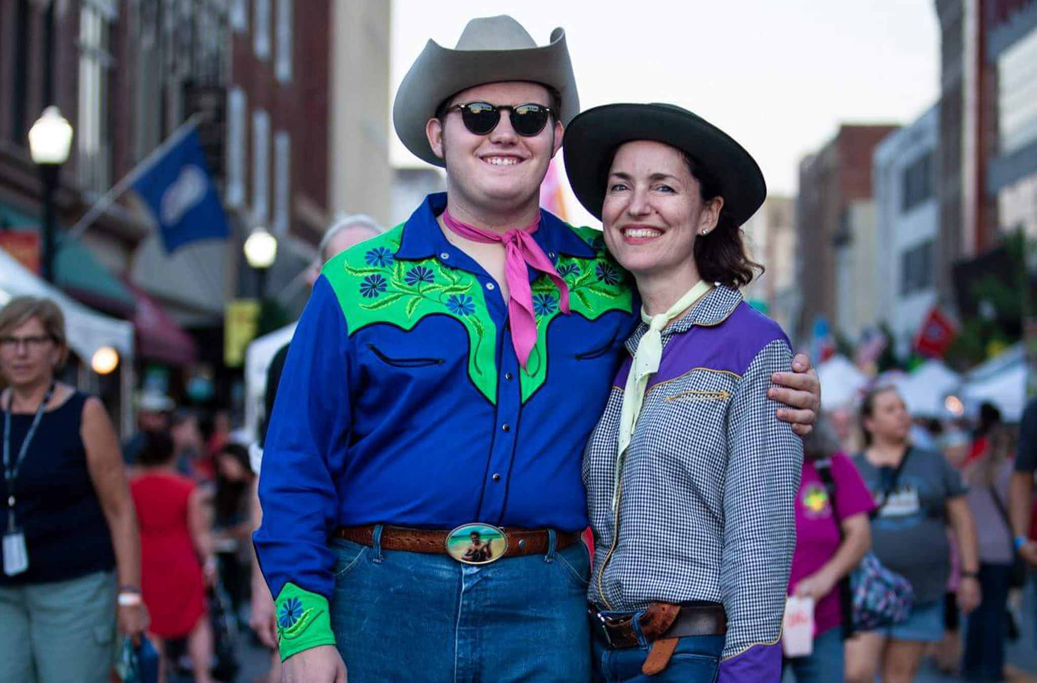 A photo of Bailey George and Jessica Stiles standing on State Street in western style clothing and cowboy hats.