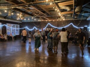 Several square dancers move around a large room with fairy lights and other fun decorations.