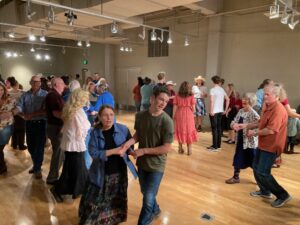 A large room with several pairs of dancers participating in a square dance.