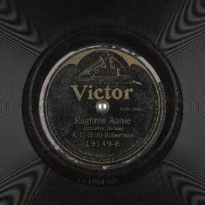 An old record with a weathered label with an image of a dog listening to an old phonograph, reading "Victor, Ragtime Annie (Country Dance), A.C. (Eck) Robertson"