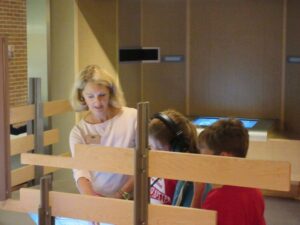 A woman guiding two children through an exhibit at the Birthplace of Country Music Museum, and explaining parts of the exhibit to them.