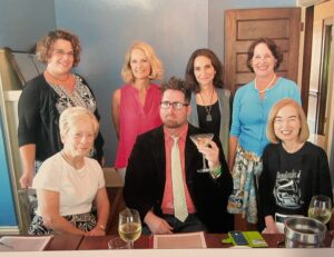 A group of women sitting around a man at a table, they are Docents and he is Thomas Richardson.