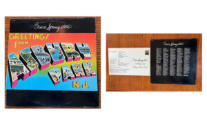 Record cover. Black band on top with Bruce Springsteen's signature in white on top and plane black bottom with a colorful greeting card image in the middle. The card fades top down from orange, yellow, green, to blue and reads "Greetings from Asbury Park N.J." The words Abury Park are filled with images of buildings and scenery.