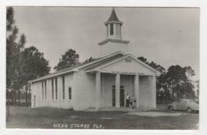 black and white image of a church with a steeple, white clapboard siding, and four pillars in front. 