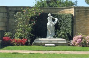 Large marble statue of a woman standing on a casket in the center of a garden. 