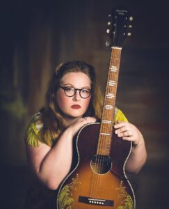 A photo of songwriter Ella Patrick posing with her guitar.