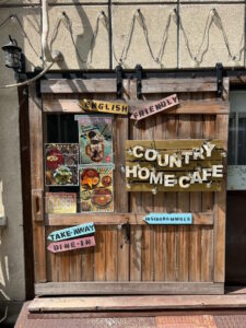 A wooden door to the "Country Home Cafe" in Osaka, Japan. On the door is pictures Japanese-American fusion food as well as signs saying "English Friendly" and "Take Away/Dine-in."